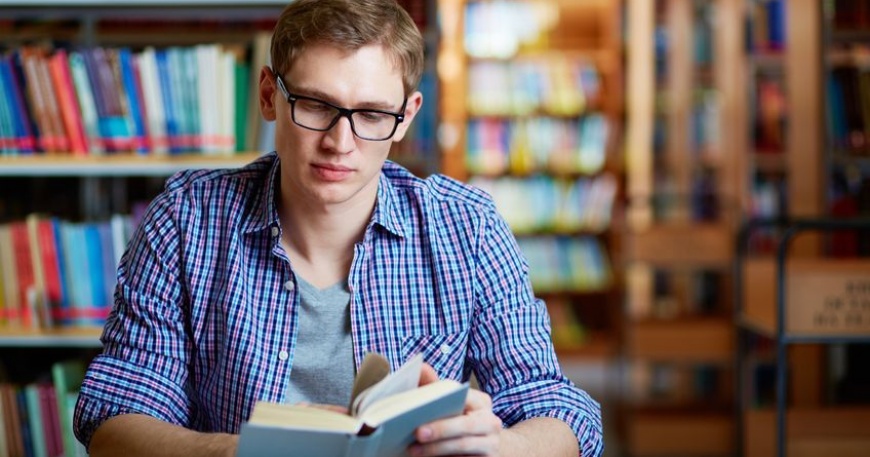 Studente che studia libro di greco antico in una biblioteca